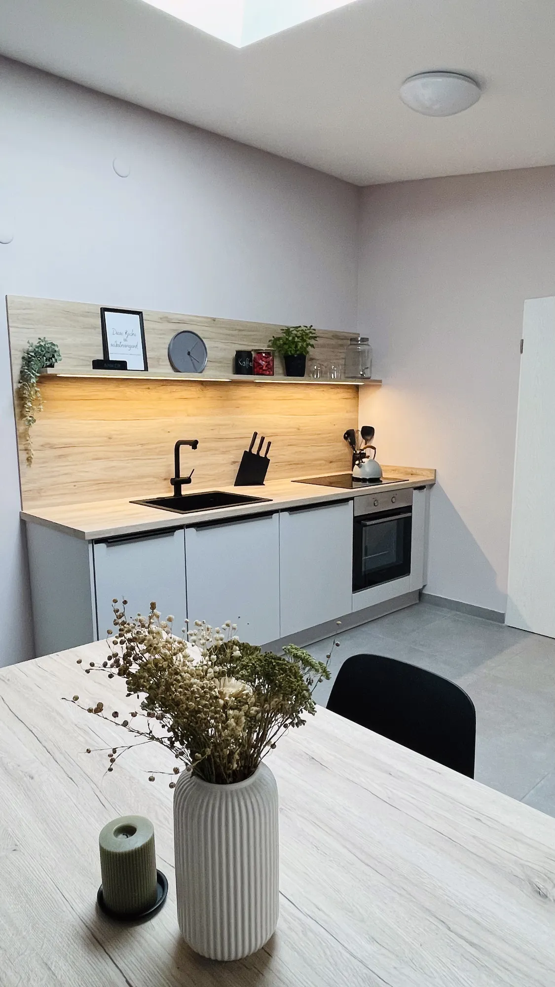 Helle Einbauküche mit Holzrückwand, Essplatz und Backofen – Referenz von SORI Studios